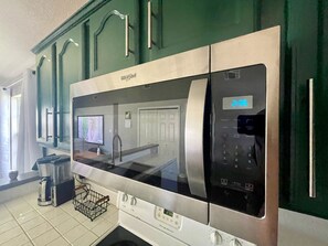 A kitchen with a stainless steel microwave oven, a coffee maker, and a small trash bin.