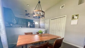A dining area with a wooden table and leather chairs, a ceiling fan, and a kitchen in the background. - Home Theatre with King Bed (Alpine)