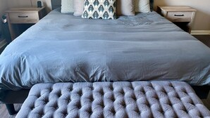A neatly made bed with a grey duvet, a grey upholstered bench, and a grey headboard. - Home Theatre with King Bed (Alpine)