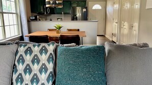 A modern kitchen with dark green cabinets, a stainless steel refrigerator, and a dining area with a wooden table and chairs. - Home Theatre with King Bed (Alpine)