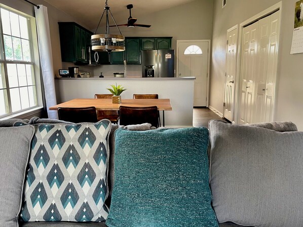 A modern kitchen with dark green cabinets, a stainless steel refrigerator, and a dining area with a wooden table and chairs.