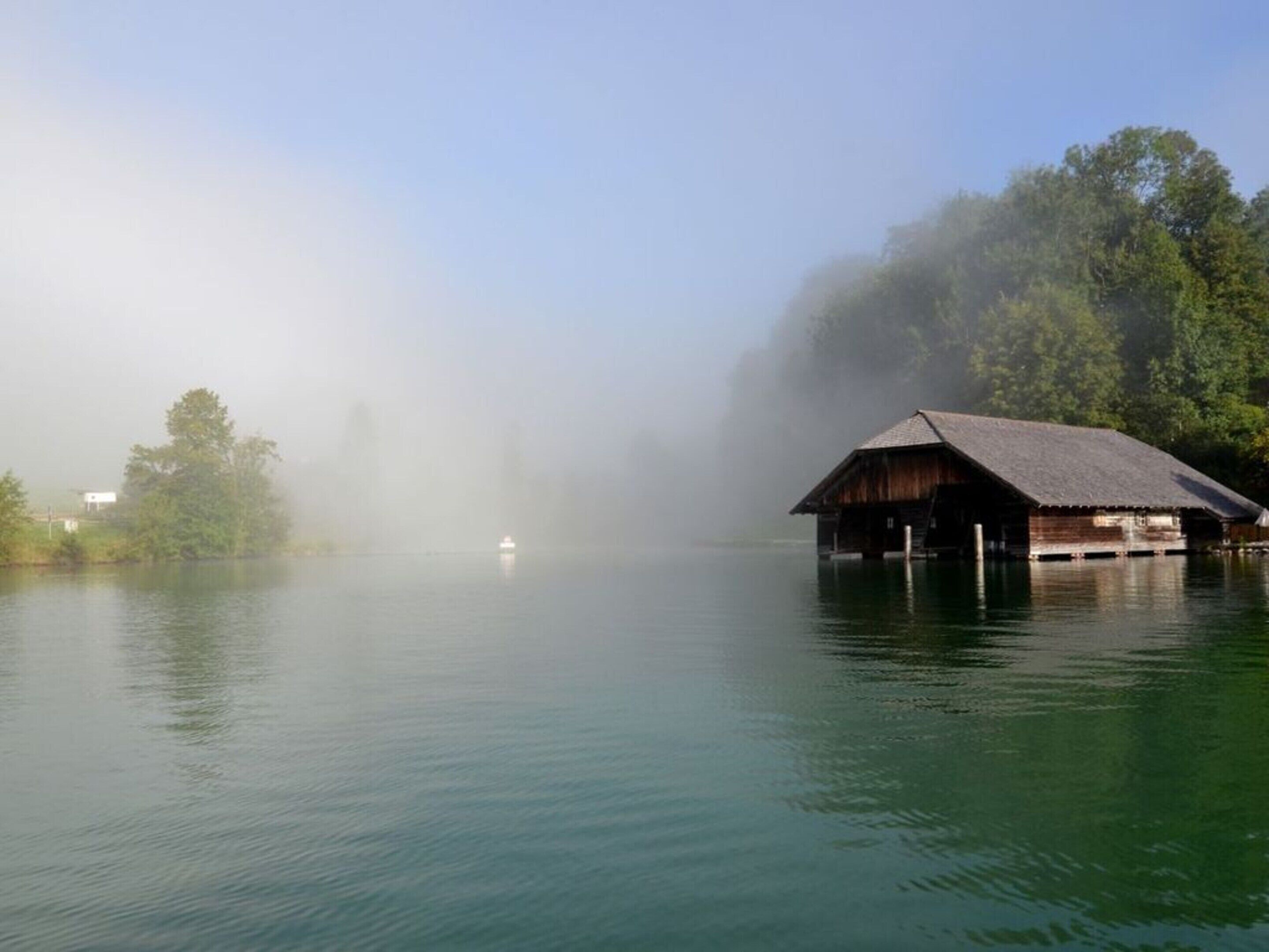 A wooden cabin on stilts over calm water, surrounded by trees and fog.