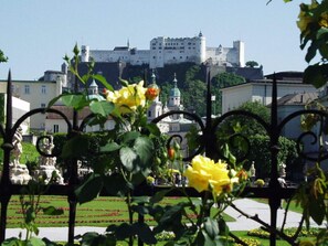 A castle with a fortified wall and a dome, surrounded by a well-maintained garden with yellow flowers and statues.