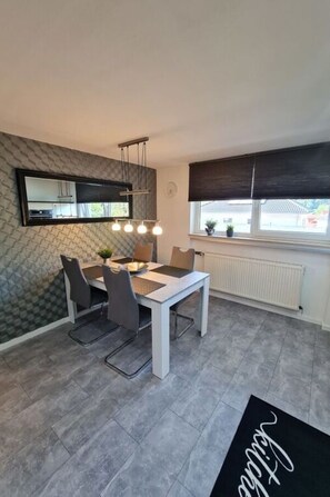 A modern dining area with a white table, grey chairs, and a pendant light. - Holiday Apartment Glockenhorn (Hinterweidenthal)