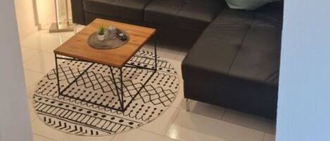 A modern living room with a black leather sofa, two green cushions, a wooden coffee table, and a patterned rug.