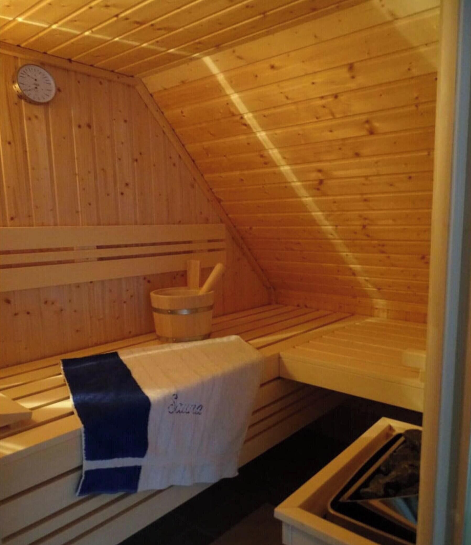 Eine Sauna mit Holzwänden und -bänken, einer Uhr und einem Handtuchhalter.