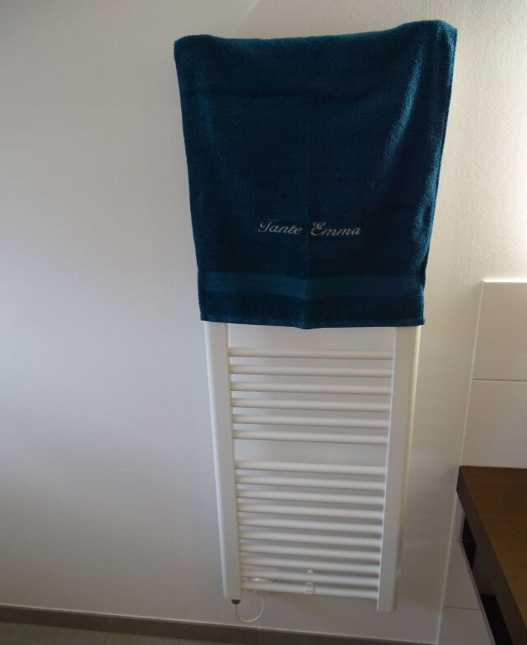 Una toalla azul oscuro colgada en un radiador blanco en una habitación con paredes blancas y suelo de madera.