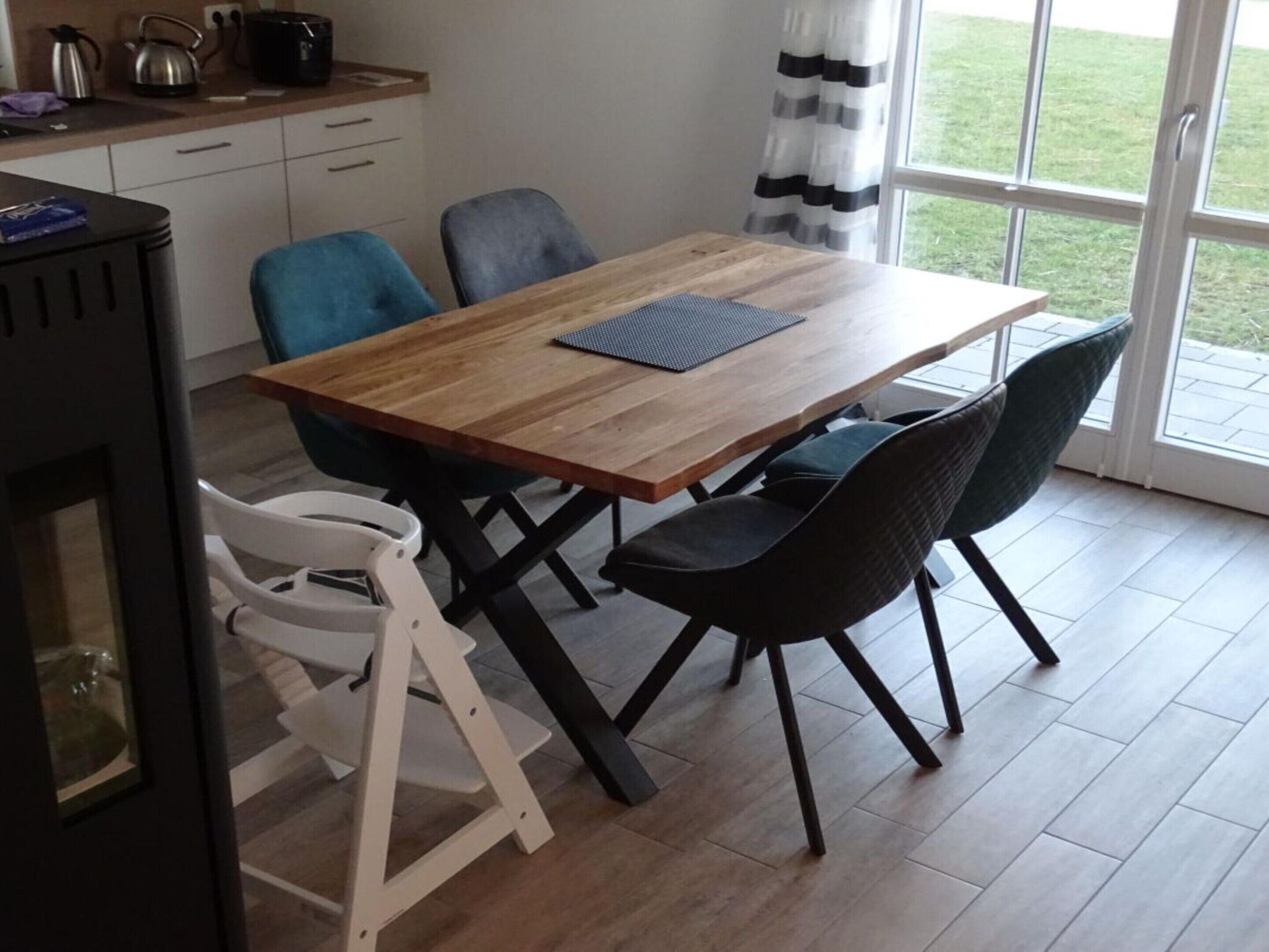 A dining area with a wooden table, black chairs, and a white chair. There is a kitchen area with a kettle and pots on the counter.