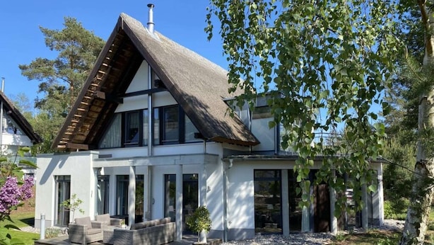 Une maison moderne à deux étages, dotée d’un toit en pente, de grandes fenêtres et d’un jardin bien entretenu.