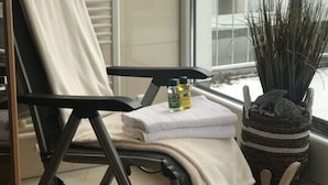 Un coin de pièce avec une chaise noire, une serviette blanche, un petit seau en bois et une plante en pot.