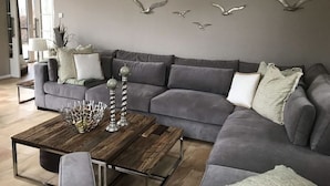 Un salon moderne avec un canapé d’angle gris, une table basse en bois et des décorations murales représentant des oiseaux.