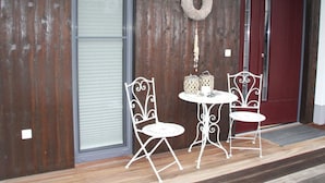 Une façade moderne avec un mur en bois, une porte rouge et un petit espace extérieur aménagé avec des chaises et une table en métal blanc.