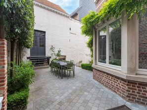 A patio with a table and chairs, surrounded by a white brick wall and greenery. - Scenic Villa in Borgloon With Garden (Borgloon)