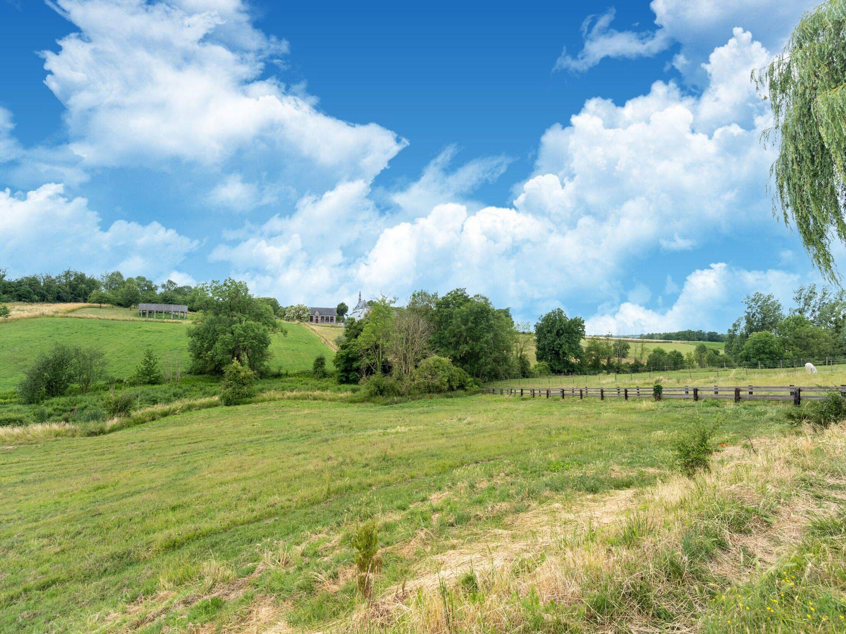 A rural landscape with a large open field, a wooden fence, and a building in the distance.