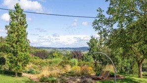 A grassy outdoor area with a wooden bench, trees, and a view of wind turbines in the distance. - Bungalow in Waxweiler Near Nature Trails (Waxweiler)