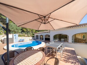 Un área junto a la piscina con jacuzzi, mobiliario exterior y un porche cubierto.