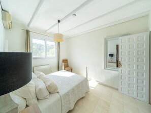 Un dormitorio con cama, una silla, un ventanal y una puerta.