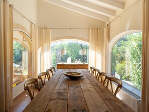 Una larga mesa de madera con sillas, un bol en el centro y vistas a la vegetación a través de amplios ventanales.