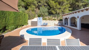 Une piscine bordée d’un muret en pierre, avec des chaises longues et un espace patio couvert.