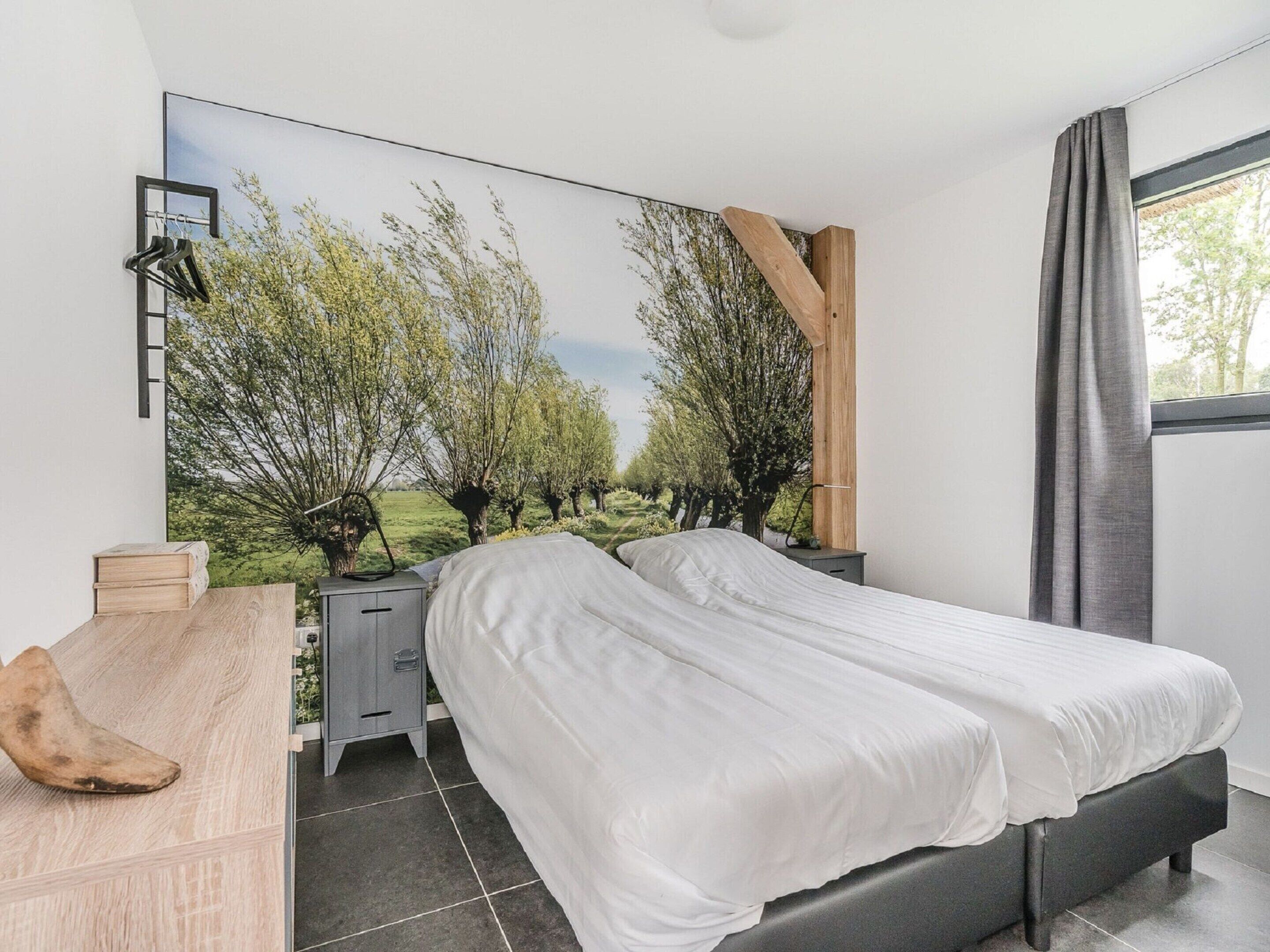 A bedroom with a bed, a nightstand, a dresser, a mirror, and a large window.