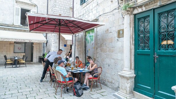 An outdoor café with tables and chairs, a green door, and a stone building facade. - Secret Apartments - One Bedroom Apartment (Dubrovnik)