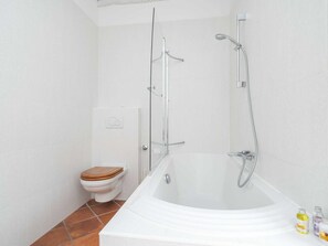 Une salle de bain avec une baignoire blanche, une douche en verre, des toilettes blanches et un sol carrelé.