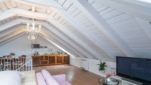 A spacious loft apartment with a high ceiling, a dining area, a kitchen, a living room with a sofa and TV, and a staircase. - Secret Apartments - One Bedroom Apartment (Dubrovnik)