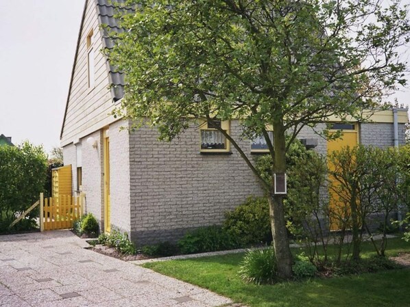 A two-story building with a brick facade, a visible window, and a tree in the foreground. - "de Zeehond" Strandslag (Julianadorp)