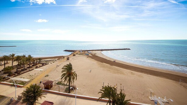 A beach with a wooden pier extending into the sea, palm trees, and a clear sky. - Belvilla by OYO Torreblanca I Primera Planta (Torreblanca)