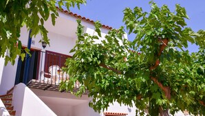 A white building with a red-tiled roof, a balcony with a railing, and a tree in front. - Belvilla by OYO Torreblanca I Primera Planta (Torreblanca)