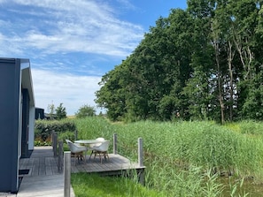 A wooden deck with a table and chairs, surrounded by tall grass and trees. - Beautiful Holiday Home With A/c, in a Holiday Park (Wemeldinge)