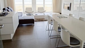 Um quarto moderno e bem iluminado com cozinha, mesa de jantar com cadeiras, sofá e uma janela grande com vista.