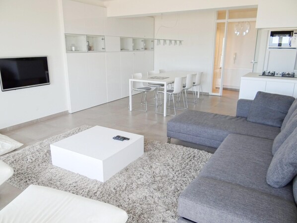 Een moderne woonkamer met een witte salontafel, een grijze bank en een televisie aan de muur.