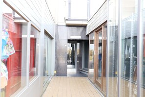 Een smalle gang met glazen deuren aan weerszijden, die uitkomt in een centrale open ruimte.