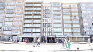 Um edifício residencial com vários andares, varandas e área comercial no térreo com lojas.