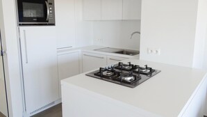 Uma cozinha moderna com armários brancos, micro-ondas embutido, fogão a gás e uma pia de aço inoxidável.