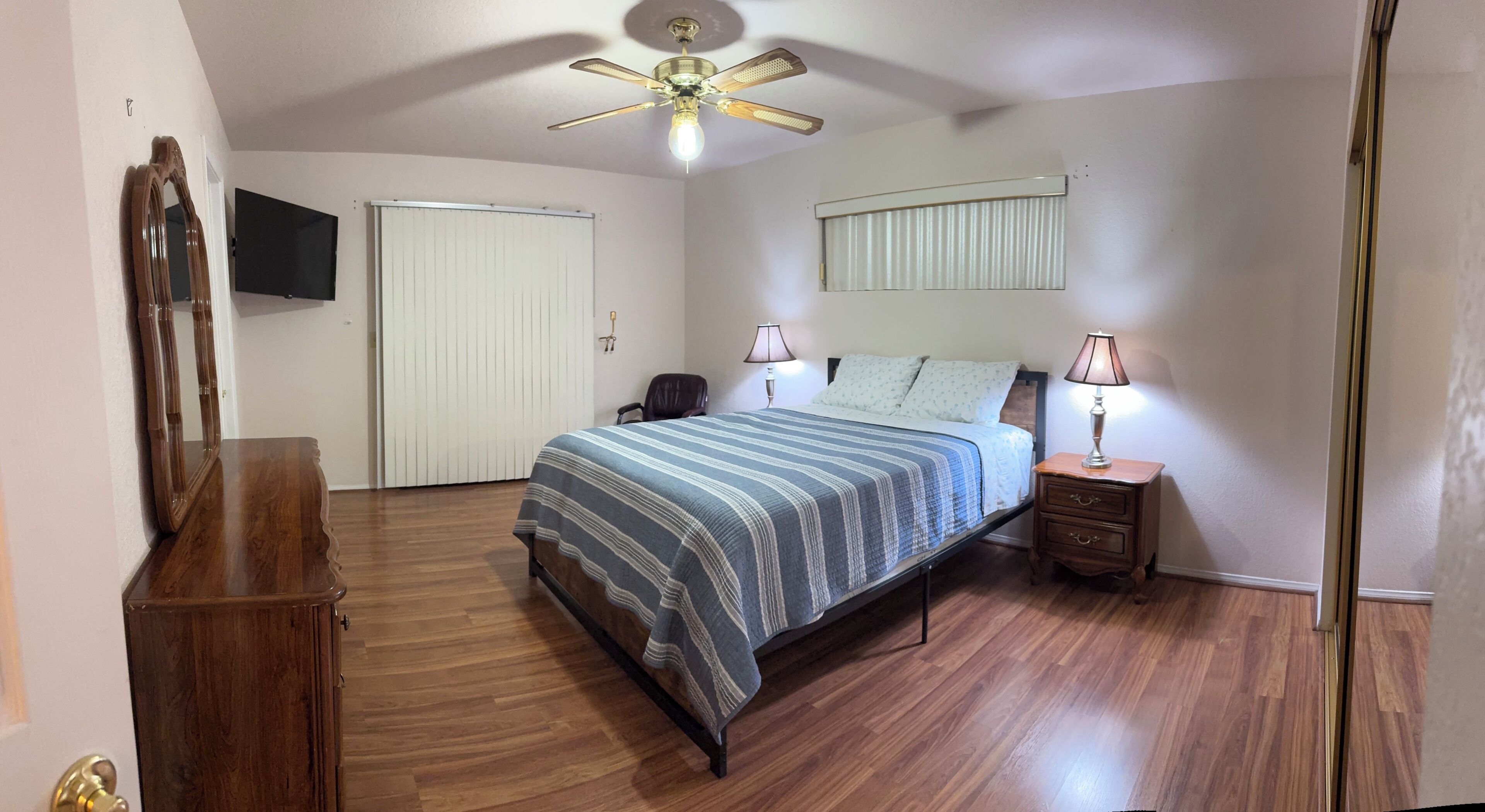 A bedroom with a bed, bedside tables, a ceiling fan, a mirror, and a wardrobe.