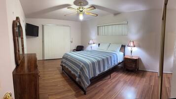 A bedroom with a bed, bedside tables, a ceiling fan, a mirror, and a wardrobe.