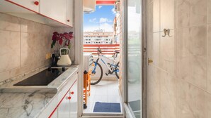 A narrow hallway with a kitchen area on one side, a bicycle in the center, and a view of buildings outside.