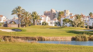 A golf course with a water hazard, palm trees, and residential buildings in the background. - Belvilla by OYO Macael (Roquetas de Mar)