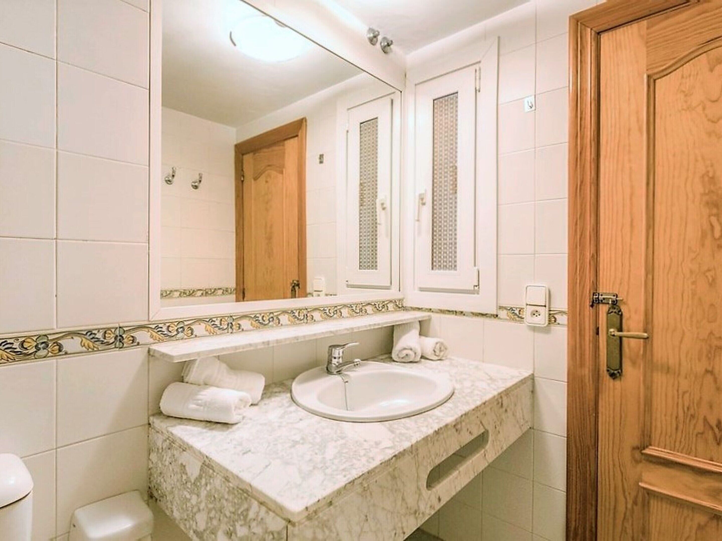 Un baño con lavamanos de mármol, dos espejos, una puerta de madera y una pared con azulejos.
