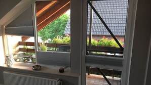 A room with a sloped ceiling, a radiator, a window with a view of a garden, and a wooden beam structure. - Seagull Modern Retreat (Wangerland)