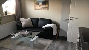 A modern living room with a black leather sofa, a glass coffee table, and a painting on the wall. - Seagull Modern Retreat (Wangerland)