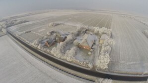 An aerial view of a rural property with several buildings, including a main house and outbuildings, surrounded by expansive fields and a snow-covered landscape.