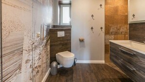 A modern bathroom with a wooden accent wall, a white toilet, a shower area, and a vanity with a mirror.