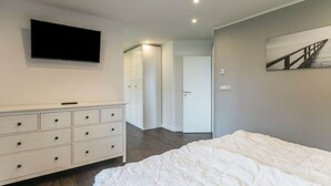 A bedroom with a bed, a dresser, a TV mounted on the wall, and a door leading to another room.