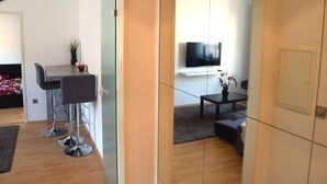 A modern living room with a TV mounted on the wall, a small table with a vase, and a sofa. There is a dining area with a table and chairs. - Cosy Apartment in Oberhausen With Balcony (Oberhausen)