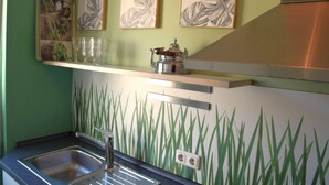 A kitchen with a green wall, a stainless steel sink, and a shelf with glassware and a kettle. - Cosy Apartment in Oberhausen With Balcony (Oberhausen)