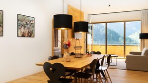 Zona pranzo moderna con tavolo in legno, sedie nere e un vaso di fiori. Due lampade a sospensione nere illuminano il tavolo.