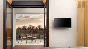 A bedroom with a bed, a TV mounted on the wall, and a sliding glass door leading to an outdoor seating area with chairs and a table.